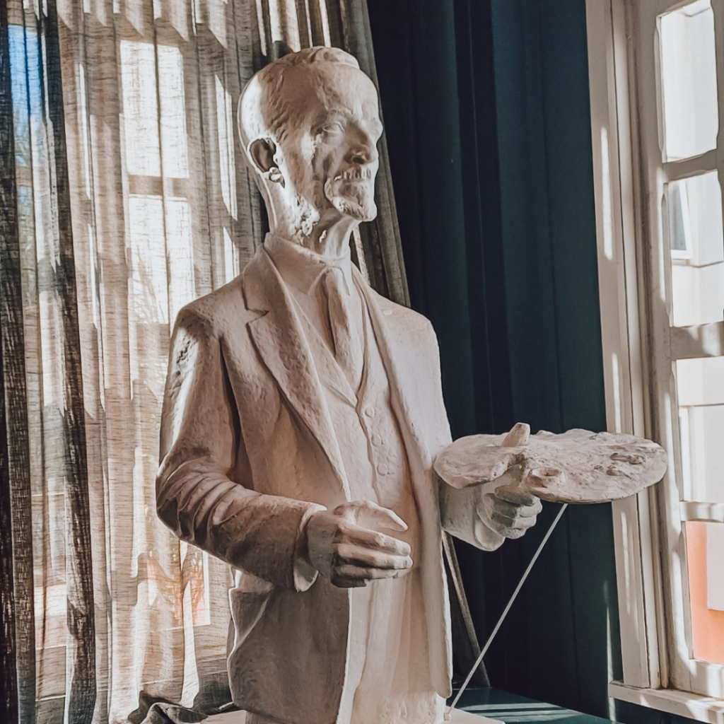Busto em gesso de homem segurando paleta de pintor, em frente à janela com cortina, no Museu Casa Alfredo Andersen em Curitiba, onde gravamos para o Onde Ver Arte