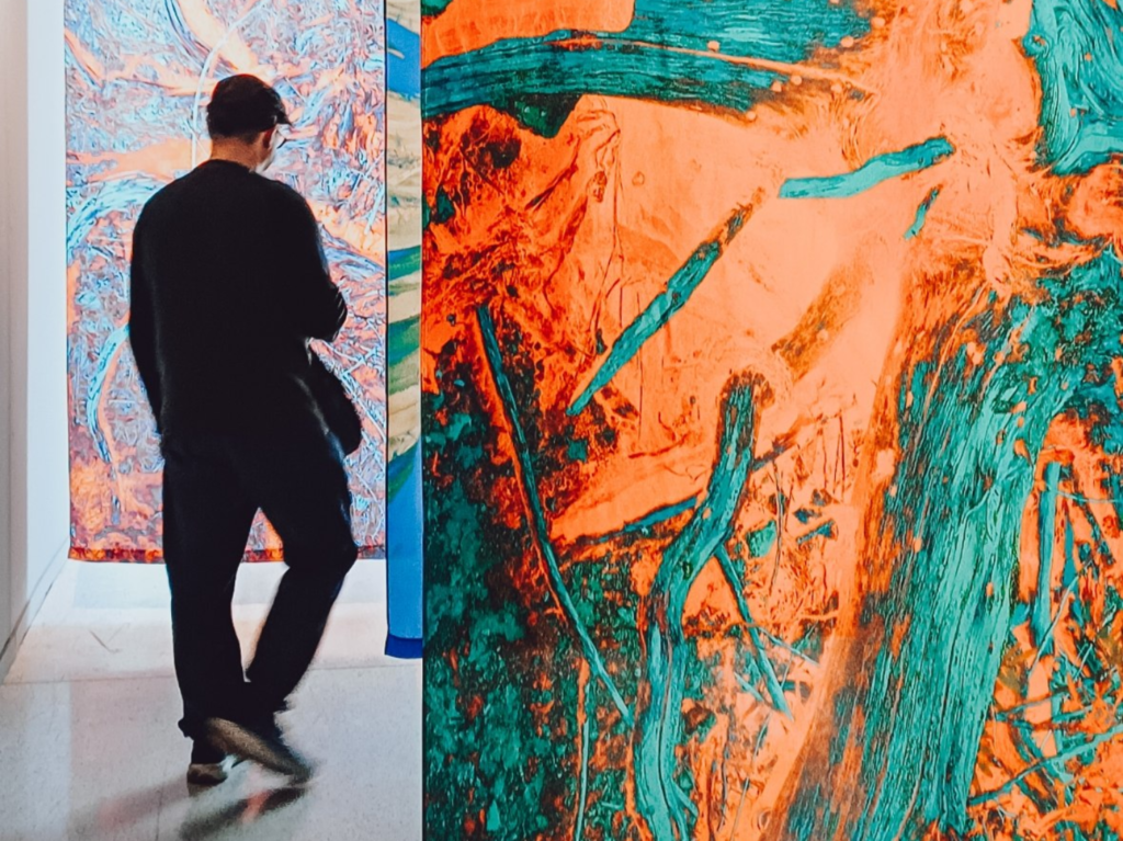 Marco atravessando uma instalação de tecidos suspensos em cores vibrantes no MON Curitiba, durante visita para o Onde Ver Arte