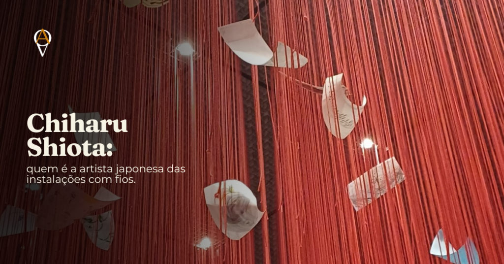 Instalação de fios vermelhos entrelaçados de Chiharu Shiota no Museu Oscar Niemeyer, em Curitiba, obra que integra a 16ª Bienal Internacional de Curitiba, com formas de papel dobrado suspensas entre os fios e pequenos pontos de luz ao fundo. Sobreposto à imagem, o texto 'Chiharu Shiota: quem é a artista japonesa das instalações com fios'.