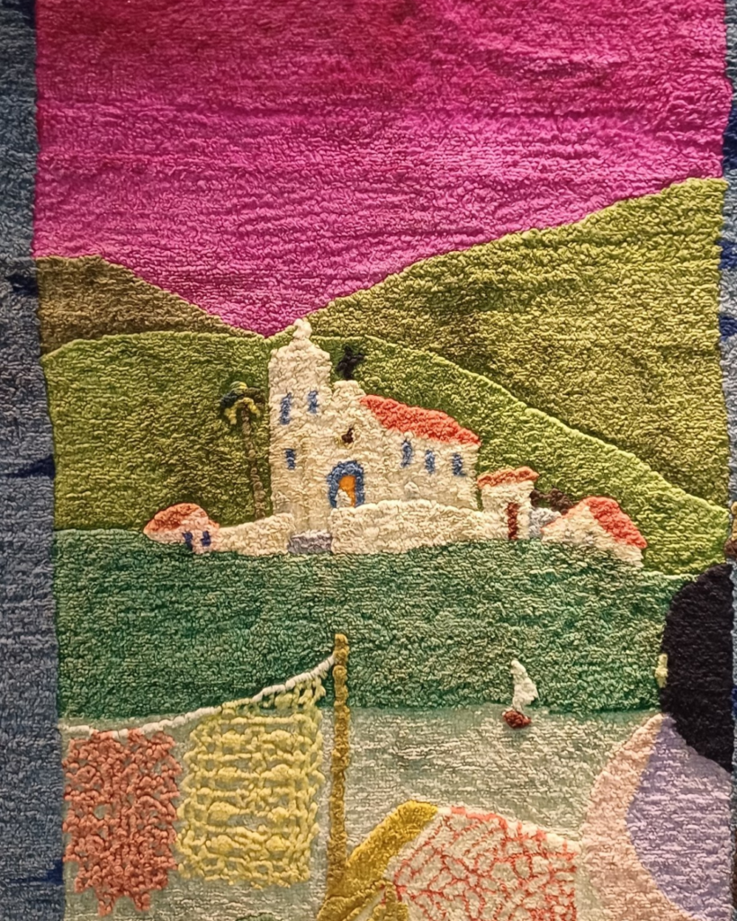 Detalhe do arco rosa do painel da direita: igreja branca de telhado laranja sobre colinas verdes, com um barco a vela pequeno na água e, em primeiro plano, redes de pesca em rosa e amarelo penduradas num varal.